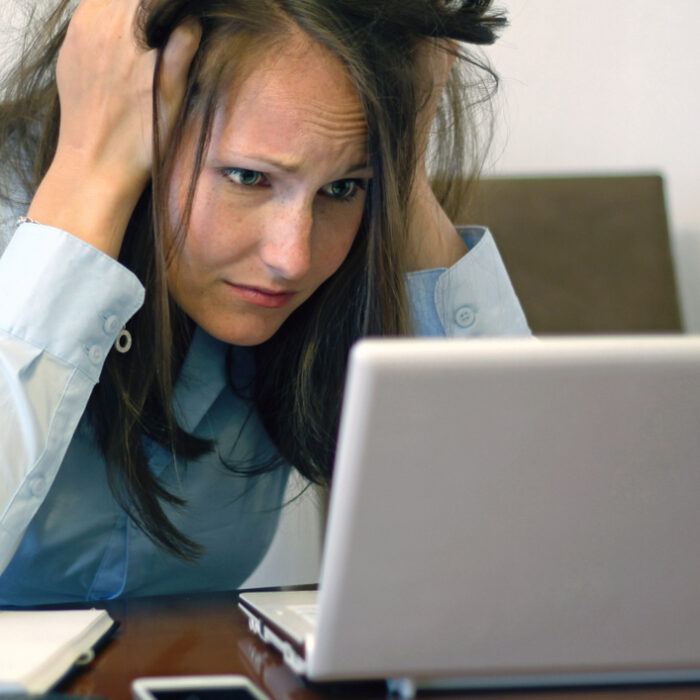 woman looking worried at a laptop screen with her hands in her hair