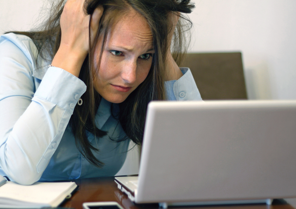 woman looking worried at a laptop screen with her hands in her hair