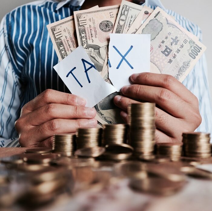man holding currency with the word "tax" on a torn piece of paper