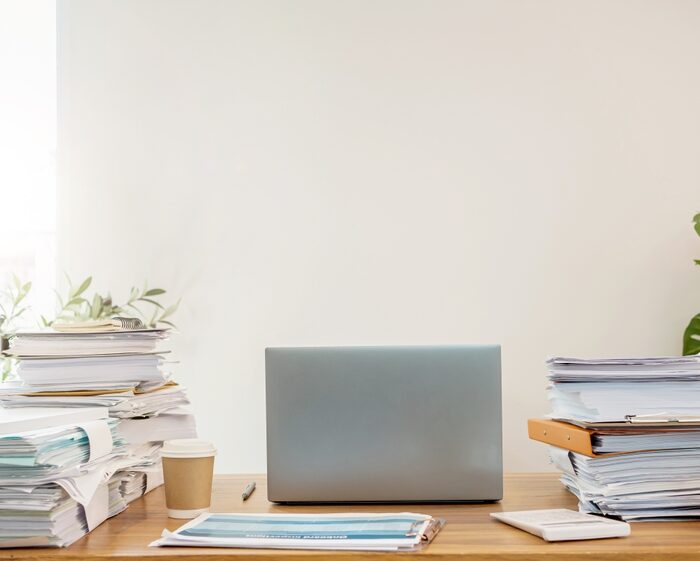 piles of paper and a laptop on a desk