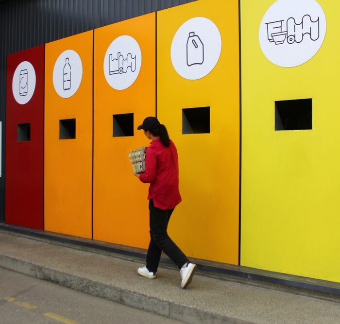 person walking in front of recycling bins