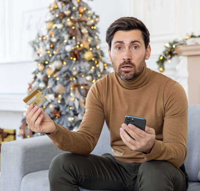 man holding a credit card and a smartphone in front of a Christmas tree