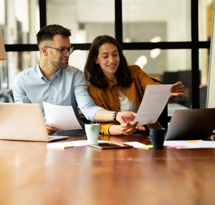 man and woman looking a paper documents and laptops