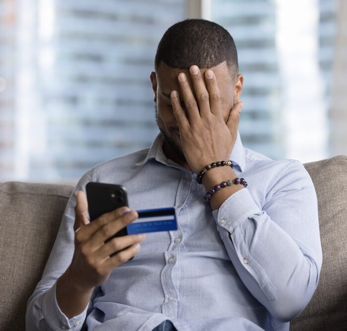 man holding a credit card and a smartphone with his hand over his face