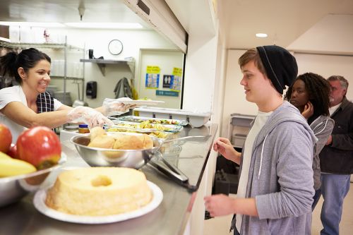 A volunteer is serving food at a homeless shelter.