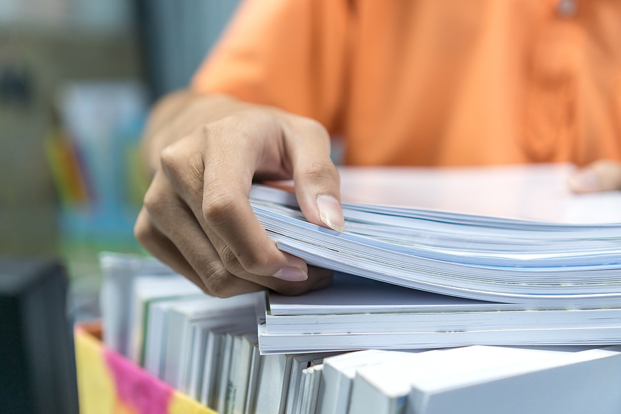 An office worker is stacking more documents onto a box filled with paperwork and folders.