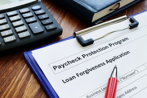 A Paycheck Protection Program loan application is attached to a clipboard sitting next to a keyboard on a desk surface.